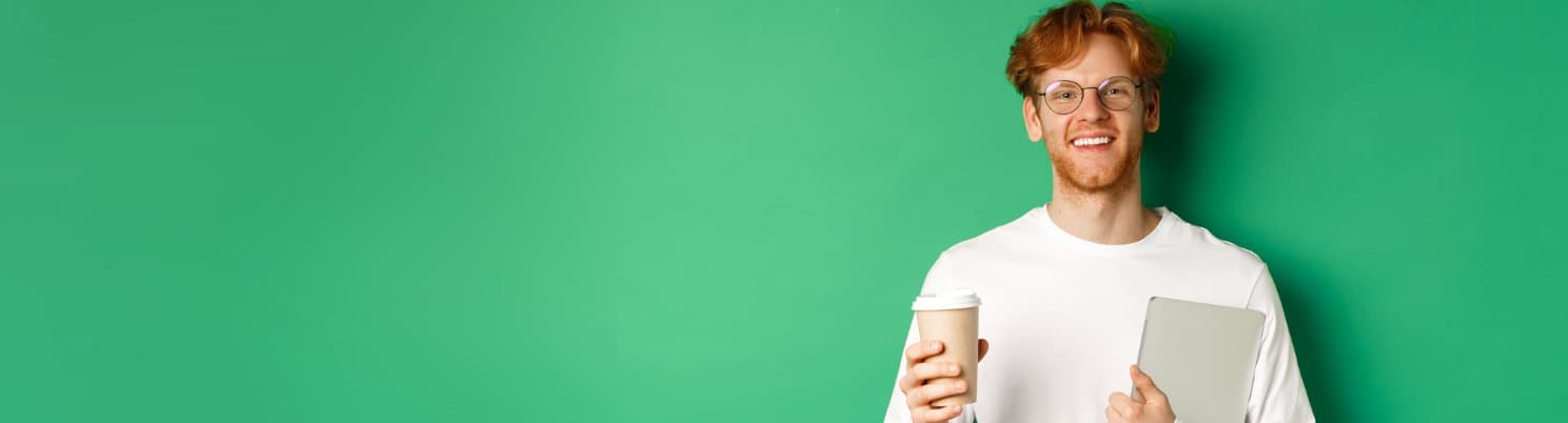 Redhead guy facing camera holding laptop and coffee, smiling