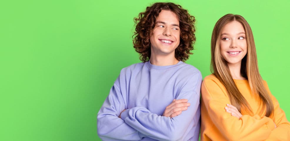 Two students standing back to back glancing over their shoulders at each other